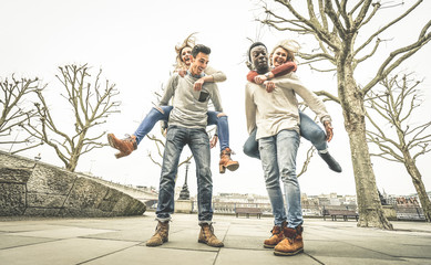 Obraz premium Happy multiracial friends couples having fun with piggiback in winter time waiting spring - Friendship concept with multicultural young people with funny attitude - Retro desaturated contrast filter