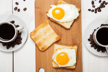 Two cups with coffee, toast and egg on a white wooden table