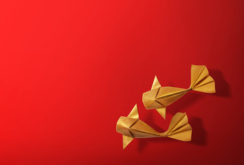 Handmade paper craft gold color origami koi carp fish on red background with empty space. 