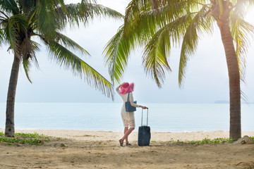 Girl tourist in bright hat and travel bag on the beach under palm trees