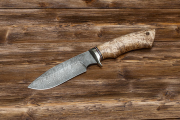 Hunting damascus steel knife handmade on a wooden background, close-up