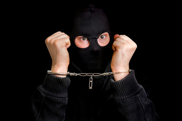 Masked thief in handcuffs isolated on black