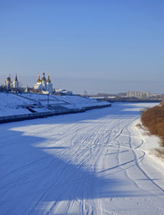 Frozen river in Siberia, Russia. Lot of ski traces in the snow. Two churches at the horizon.