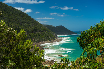 Turquoise Sea at Great Ocean Road. View at beginning of famous "Great Ocean Road" South Australia. Bushes in the foreground, turquoise wavy waters in the middle, green bushy mountains in the backgroun
