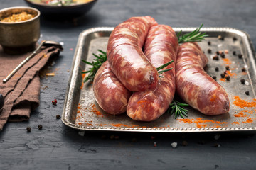 Raw sausages grilled on a iron tray on dark surface