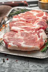 Three raw pork steaks on iron tray on light surface