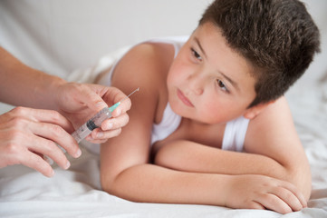 little fat boy looks at doctors hands with a syringe