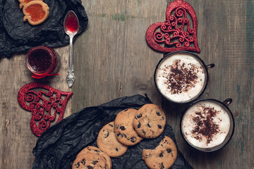 Romantic breakfast. Two Cups of coffee, cappuccino with chocolate cookies and biscuits  near red hearts on wooden table background. Valentine day. Love. Top view.