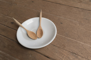 Together wood spoon in white plate on wooden table in the coffee shop.