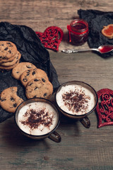 Fototapeta na wymiar Romantic breakfast. Two Cups of coffee, cappuccino with chocolate cookies and biscuits near red hearts on wooden table background. Valentine day. Love. Top view.