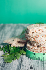 Pieces of crispbread near measuring tape and green arugula on grey background. Diet concept. Healthy food.