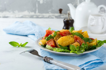 Fried cheese slices in corn grits, cooked tomatoes and lettuce on a light background. breakfast concept. Selective focus.