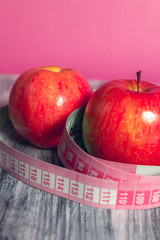 Two red apple with measuring tape on pink background. Healthy diet concept. 