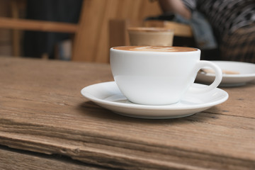 White cup of coffee on wooden table in the coffee shop.