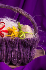 Easter egg decorative in twine in purple basket on wooden table on purple background.