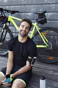 Laughing cyclist sitting by bicycle, portrait