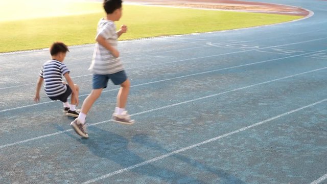 Young Asian boy running on blue track, fall and help by another boy.