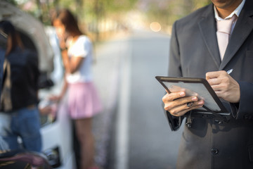 device in hand of insurance agent on line report the damaged of both cars to the office during serious and worry of both drivers are in background