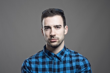 Moody portrait of skeptical young man frowning face looking at camera over gray studio background. 