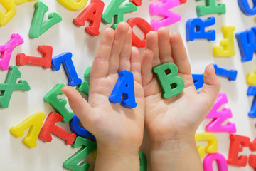 Naklejka premium Little girl learning to read using magnetic letters holding in hands a and b. Learn Study Education School Knowledge Concept