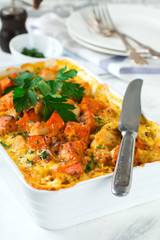 Baked pumpkin with chicken, spices and cream sauce in a white ceramic form on a light background. Selective focus.
