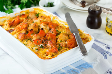 Baked pumpkin with chicken, spices and cream sauce in a white ceramic form on a light background. Selective focus.