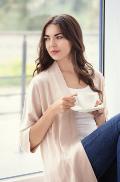 Beautiful woman with cup of aromatic coffee sitting near window