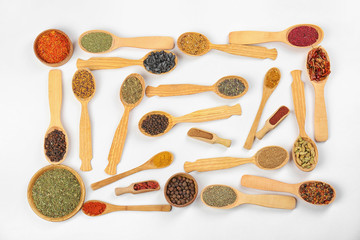 Different spices in wooden spoons on white background