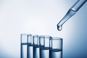Closeup of a pipette dropping a sample into a test tube on grey background