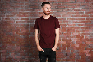 Young handsome man in claret red T-shirt on brick wall background