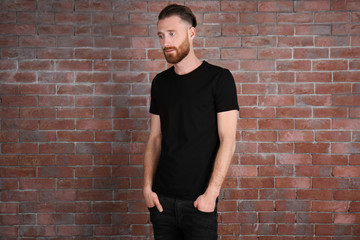 Young handsome man in black T-shirt on brick wall background