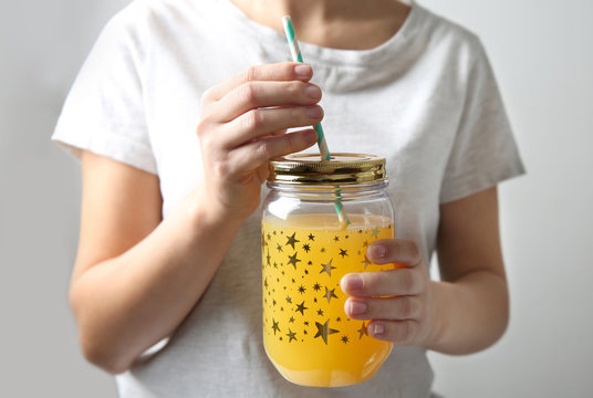 Young woman holding glass jar of orange juice, closeup