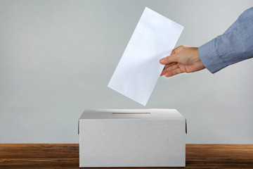 Male hand putting voting ballot into the box  on color background