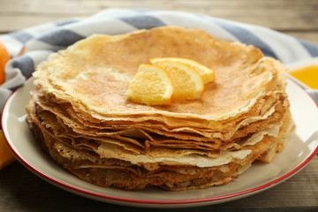 Stack of delicious pancakes with orange on wooden table
