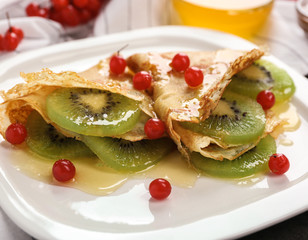 Delicious pancakes with kiwi and viburnum on white plate