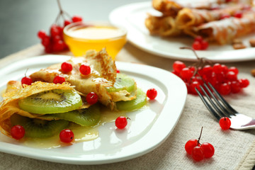 Delicious pancakes with kiwi and viburnum on white plate