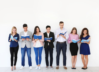 Fototapeta premium Group of people reading books while standing near light wall