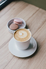 Cup of coffee cappuccino and french dessert macarons standing near window