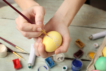 Female hands painting Easter eggs on wooden table