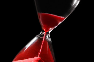Time passing concept. Crystal hourglass with red sand on black background