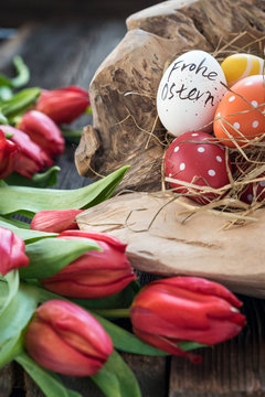Ostereier in einer Holzschale mit einem Strauss roter Tulpen