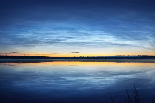 Bright noctilucent clouds over a lake in Latvia on a summer night