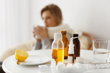 Lemon, medicines and electronic thermometer with blurred ill woman on background