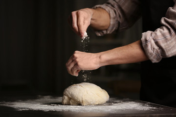 Man sprinkling flour over fresh dough on kitchen table