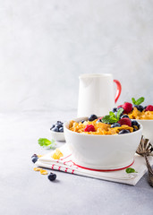 Corn flakes with berries and milk on light gray background. Copy space. Healthy breakfast concept.