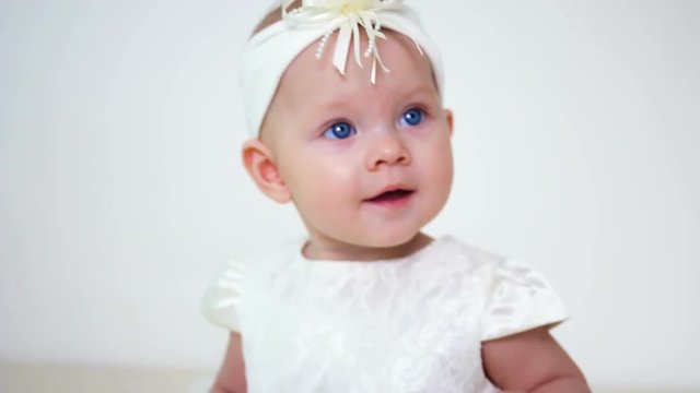 baby girl in white dress and headband sitting on a little iron bed