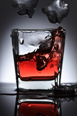 Glass of whiskey with falling ice on a black background