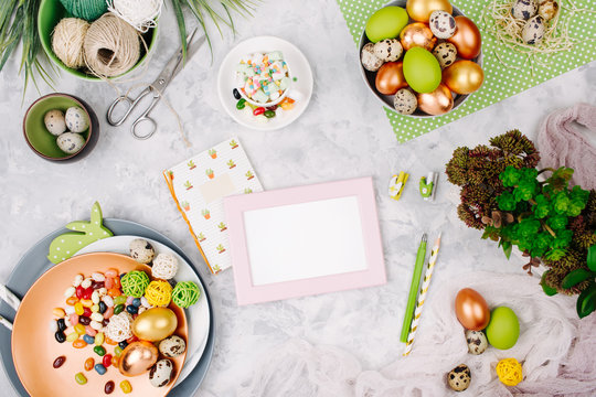 Workspace with notebook,  photo frame and  easter decoration: Painted eggs in trays, candy, succulents with copy space. Holiday background. Flat lay, top view