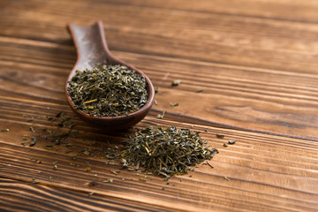 cup of green tea and spoon of dried green tea leaves on wooden background