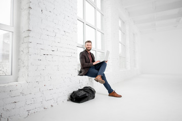 Elegant businessman sitting on the window with laptop in the white office interior